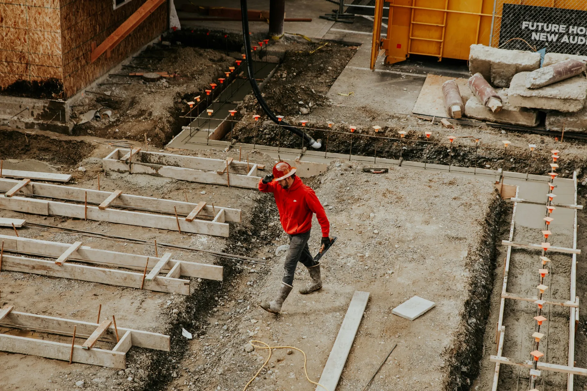 Excavation around a house foundation, showing a black waterproof membrane being applied to the exterior wall.