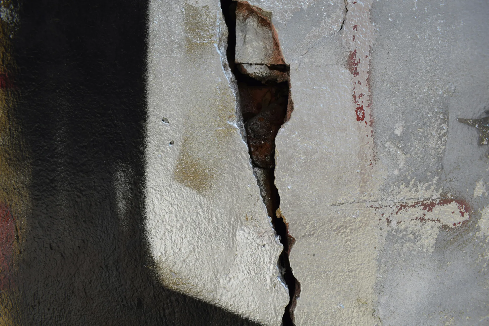 A foundation repair specialist inspecting a crack in a concrete basement wall with a flashlight, highlighting the source of a water leak.
