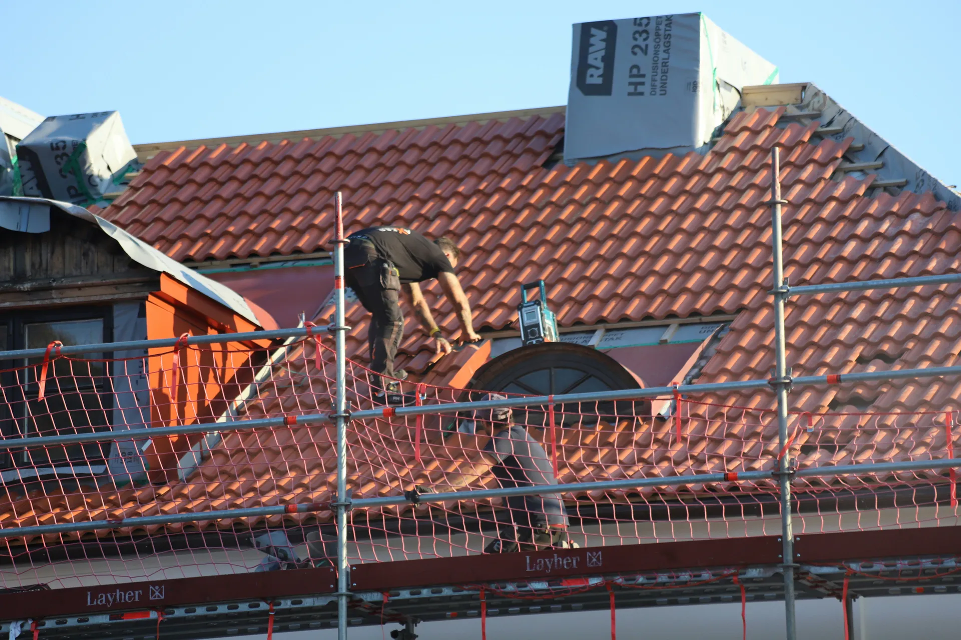 A licensed NJ roofing contractor on a roof in a New Jersey suburban neighborhood, inspecting shingles for leak damage.
