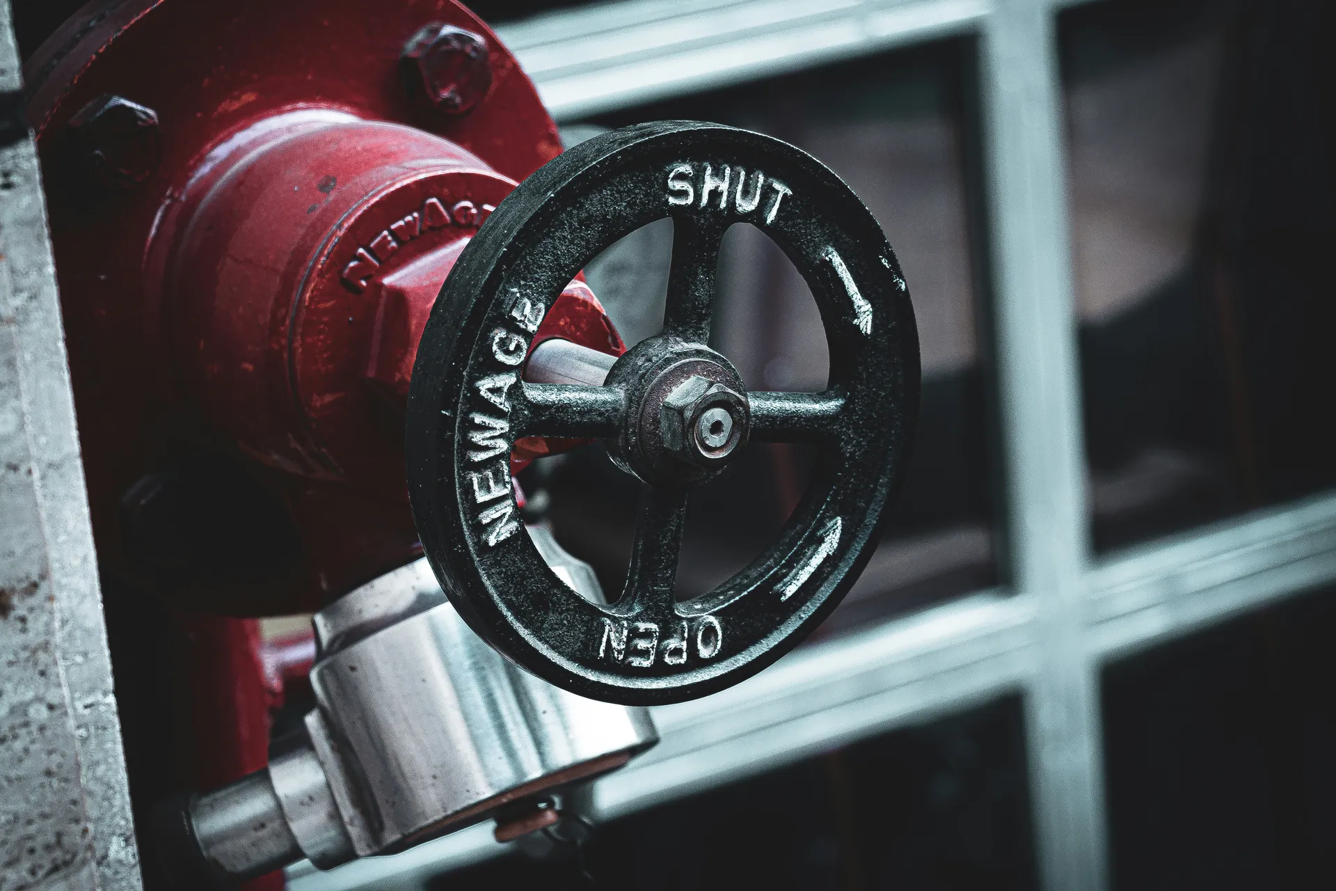 A hand turning a red main water shutoff valve to the fully open position.