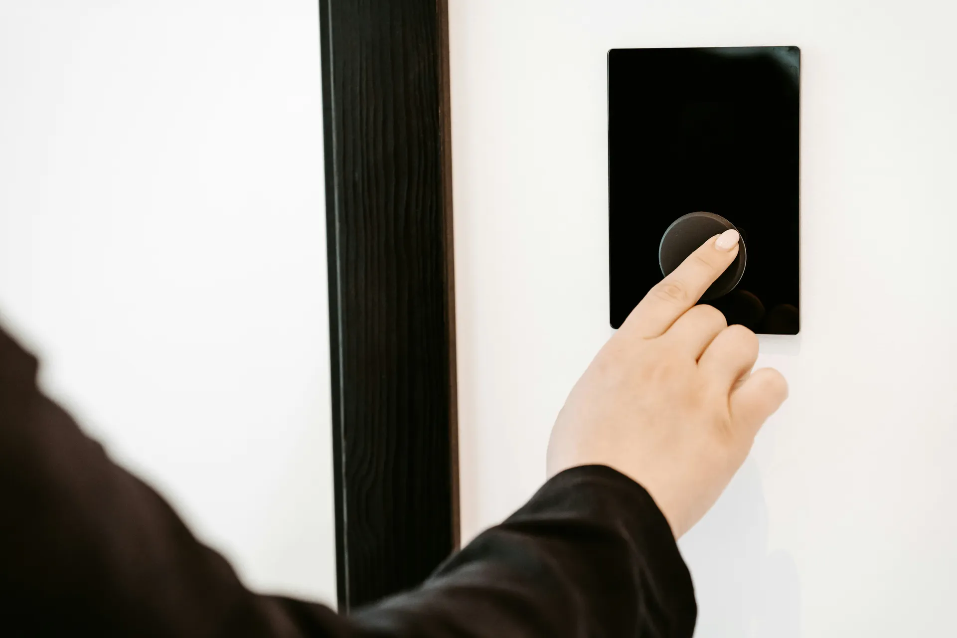 A person's hand adjusting a smart thermostat mounted on a clean, white wall.